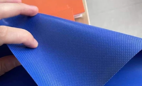 Close-up of blue PVC tarpaulin held by hand – durable, waterproof, from trusted tarpaulin supplier.